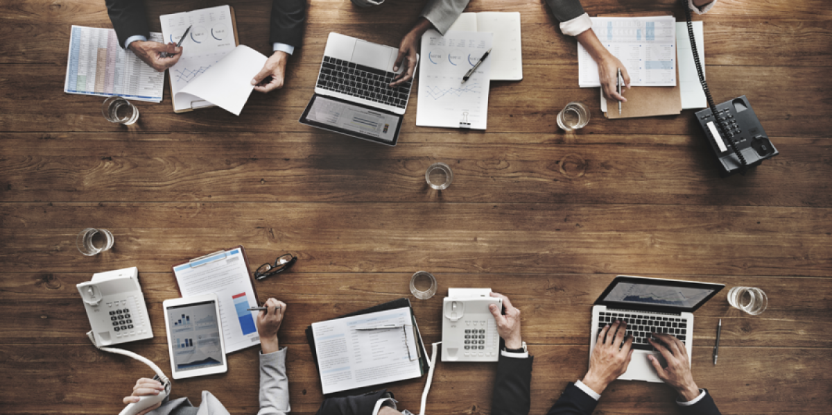 Overhead view of an investment team working across laptops and printed research during diligence